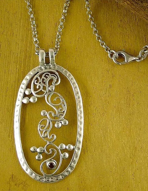 Elegant, oval pendant with four dancing paisley motifs and a garnet accent